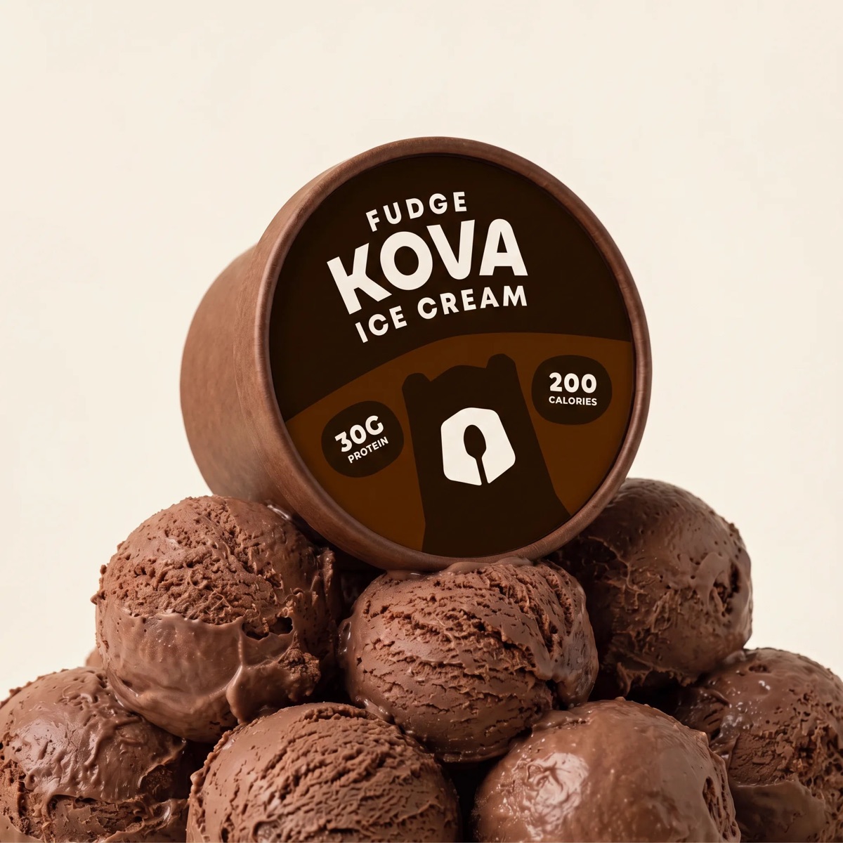 A brown Kova Fudge cup tilted forward on a mound of chocolate scoops, the die-cut lid facing the camera.
