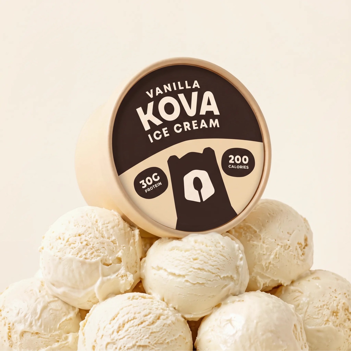 A cream Kova Vanilla cup tilted forward on a mound of vanilla scoops, the die-cut lid facing the camera.